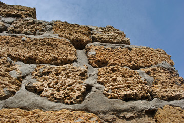 Crimean coquina rock blocks with cement ruined farm wall close up texture, blue sky background