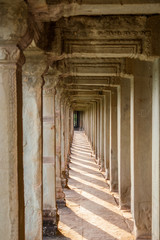 Fototapeta na wymiar Inside the outer corridor of Angkor Wat, Siem Reap, Cambodia. The columns cast their shadows on to the floor made of big stone slabs.