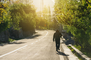 a man with backpack walking alone on empty road in the morning with bright sunlight