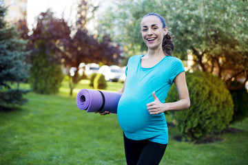 Sports for moms. Beautiful smiling young pregnant woman in sportswear comes with a karemate in hands