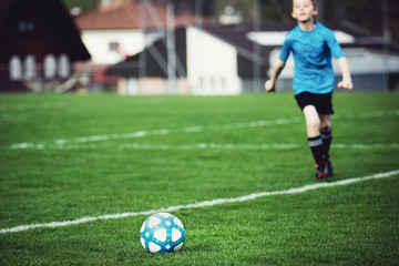 Boy playing soccer at local stadium outside on grass field running to kick the ball. Lower shot,...