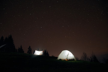 Fototapeta na wymiar Camping under the stars at night in mountains, Illuminated tents