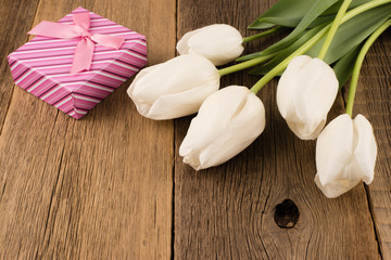 White tulips with gift on old wooden table.