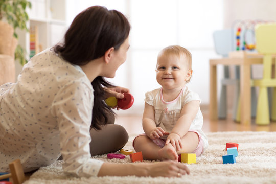 Nanny or babysitter looks after kid toddler. Baby girl playing with educational toys in nursery. Child having fun with colorful different toys at home.