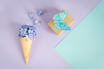Ice cream horn or cone with purple hyacinth on a purple -mint background with gift boxes and butterfly.  Floral minimalism, greeting card. Top view, place for text.