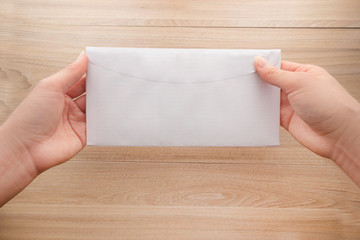 Obraz premium Woman's hand holds a white long paper envelope or letter envelopes on a wooden desk, Top view background.