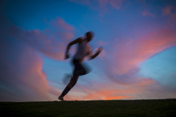 Fototapeta na wymiar Colorful sunset view of a silhouette of a man running with motion blur. Slow shutter speed to enhance sense of movement.