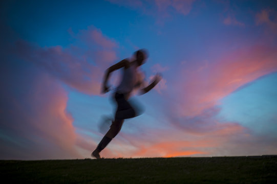 Colorful Sunset View Of A Silhouette Of A Man Running With Motion Blur. Slow Shutter Speed To Enhance Sense Of Movement.