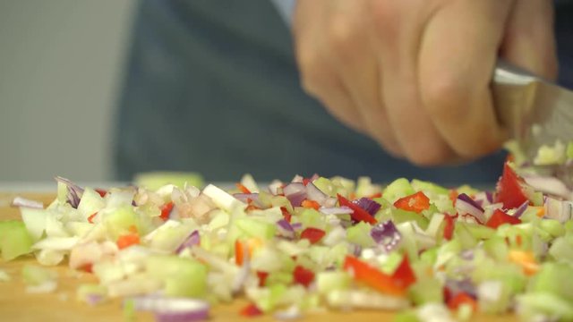 man chopping fast fresh celery, red pepper and onion on wooden board with sharp knife close up