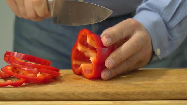 Closeup of hands of chef cook cutting red pepper on wooden table
