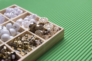 Clothes buttons in wooden box on green cardboard background