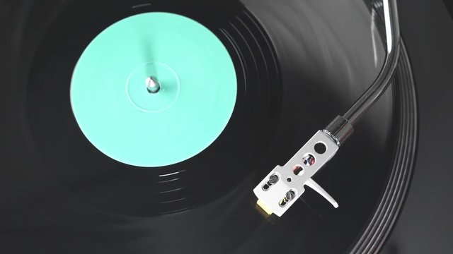 The vinyl record on DJ turntable record player close up. Black vinyl background with a green screen in the center. The rotating plate and stylus with the needle close-up. Loop. Macro. View from above