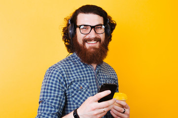 happy smiling bearded man with eyeglasses and headphones using phone and looking at the camera. Coffee to go