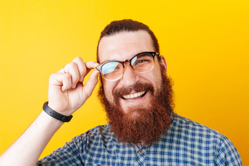 Joyful bearded man wearing blue shirt and eyeglasses over yellow background - obrazy, fototapety, plakaty