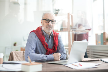 Portrait of mature businessman in eyeglasses sitting at his table at office