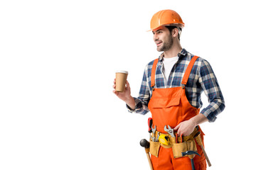 Smiling builder in orange overall and tool belt drinking coffee isolated on white
