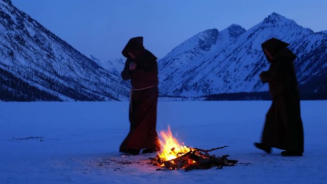 Group of monks in brown cloaks of the order of St. Francis are circling around the fire