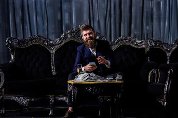 Fototapeta na wymiar Millionaire in elegant suit smokes and drinks on luxurious sofa.