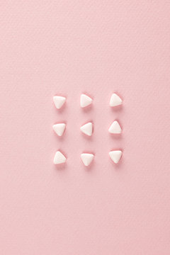 Triangular pills ordered in rows on pink background