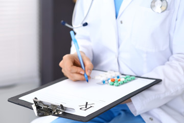 Doctor writing prescription form while sitting at chair in hospital, closeup view.  Physician finished examining his patient and prepare treatment program. Healthcare, insurance and excellent servic