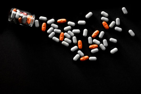 Pills spilling from bottle on black background