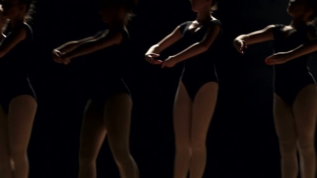 Close-up silhouette of small flexible ballerinas on a black background. Children are engaged in ballet in ballet class in the dark.