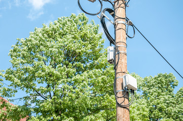 Electric wires on wooden street pole with internet or cell phone communication boxes and blue sky...