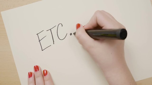 Girl hands writing etcetera in capital letters and suspension periods on a white paper with black marker
