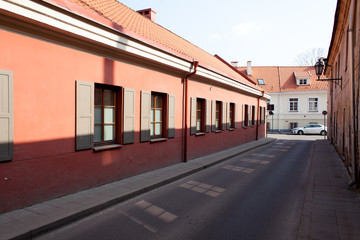 Empty narrow European street. An old street with paving stones on the ground and red buildings with windows and shutters on a clear sunny day