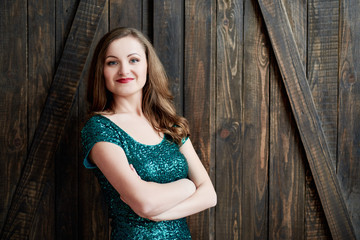 Fototapeta premium Beautiful smiling young woman in emerald dress standing with crossed arms on wooden background, copy space. St. Patricks Day, March 17