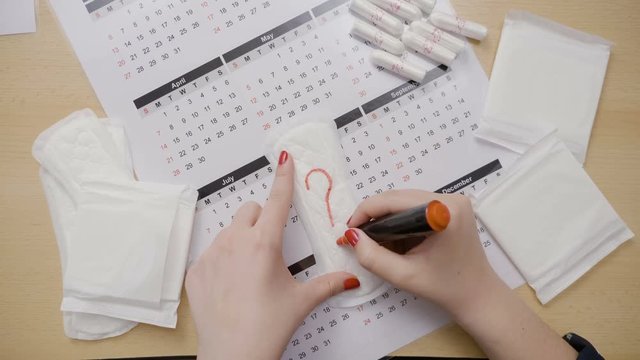 Teenage girl counting the days of her last ovulation and drawing question marks on tampon calendar and asking why her period is running late