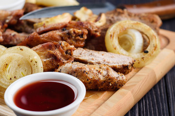 Mixed fresh grilled meat with onion, mushrooms and sauce on wooden cutting board. Assorted delicious barbecue meat with vegetables from summer BBQ. Healthy eating