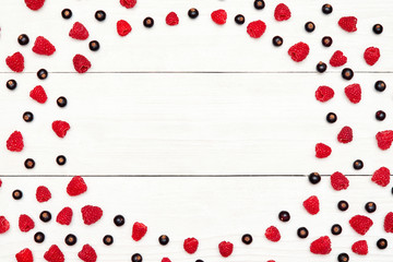 Circle frame from ripe sweet raspberries and black currants, free space. Fresh berries on white wooden background. Summer, healthy food concept. Berries background