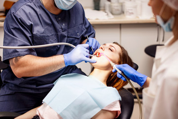 Male dentist treating teeth to young woman patient in clinic.