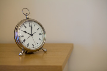 Table iron white clock on a wooden shelf against a blurred white wall
