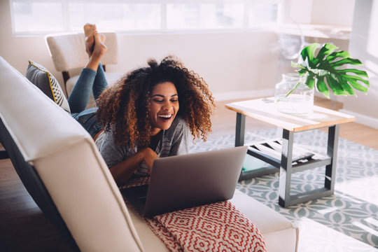 Smiling woman using a laptop while lying on the sofa