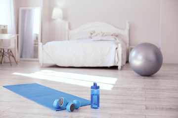 Sports equipment. Blue small dumbbells lying on the yoga mat while water bottle standing next to it