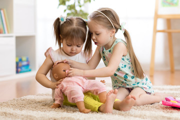 Two children girls playing doctor with a doll in kindergarten