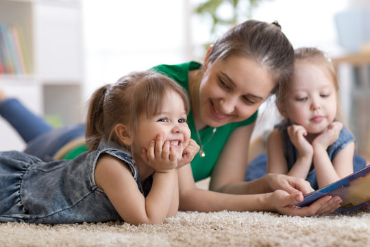Children laughing and having fun reading stories with their mother laying on floor at home