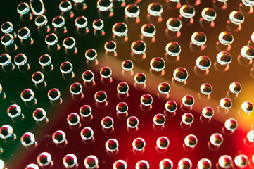 Round drops of water on a glass surface, in which a background of colored triangles is reflected.