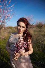 Naklejka premium Young woman in a dress walking among peach trees