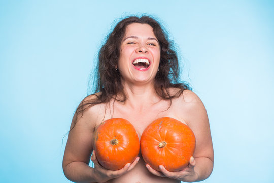 Young happy woman holds pumpkin in hands above her breast. Plastic surgery and silicone implants concept.