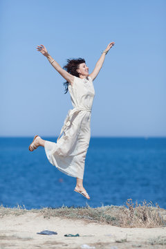 Middle aged woman jumping against sea with arms raised
