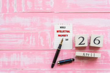 World Intellectual Property Day April 26, Wooden Block calendar note book and black pen on pink Pastel wooden table background texture.