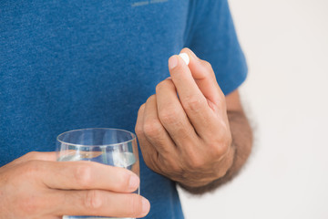 medicine, health care and people concept - close up of man taking in pill and another hand holding a glass of clean mineral water.