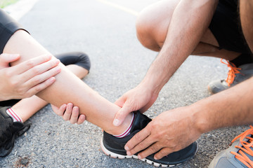 Ankle sprained. Young woman suffering from an ankle injury while exercising and running and she getting help from man touching her ankle. Healthcare and sport concept.