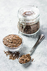 Flax seeds in glass jar, bowl and spoon on concrete background. Selective focus, space for text.