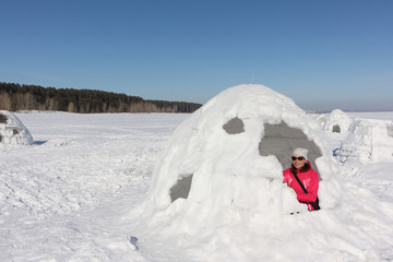 Happy woman in a red jacket sitting in an igloo   on a snowy glade