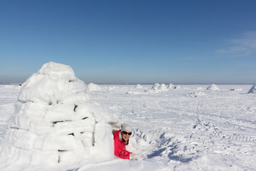 Happy woman in a red jacket lying in an igloo   on a snowy glade