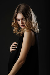 Sensual young woman with beautiful make-up and curly blonde hair posing in the studio isolated on black background. Side fashion portrait